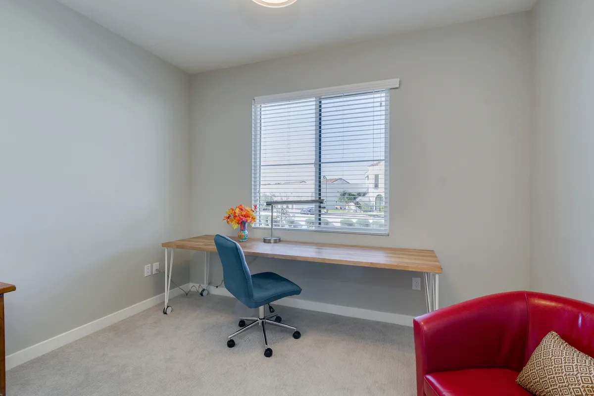A bright workspace featuring a modern desk and chair positioned by a large window, accented with a vibrant red chair and a fresh flower arrangement. Natural light streams in, creating an uplifting and focused environment ideal for work or study.