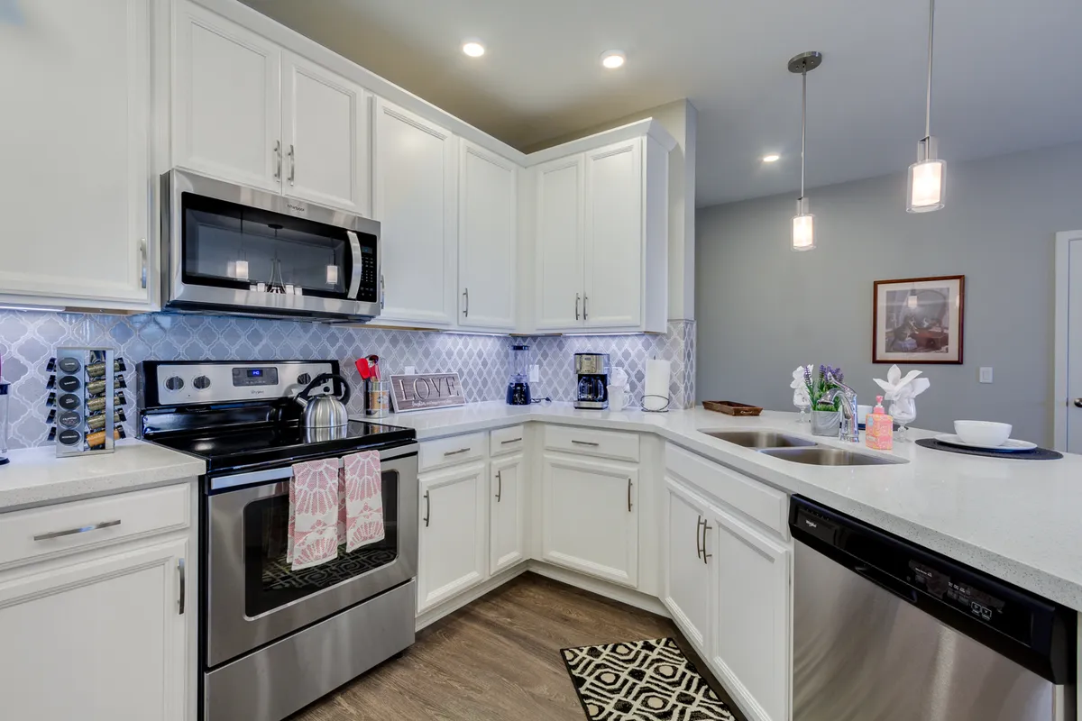 A stylish, sunlit kitchen boasting stainless steel appliances, gleaming quartz countertops, a decorative backsplash, and inviting kitchen accessories. The breakfast bar offers a casual dining option and seamlessly connects to the open-plan living area.
