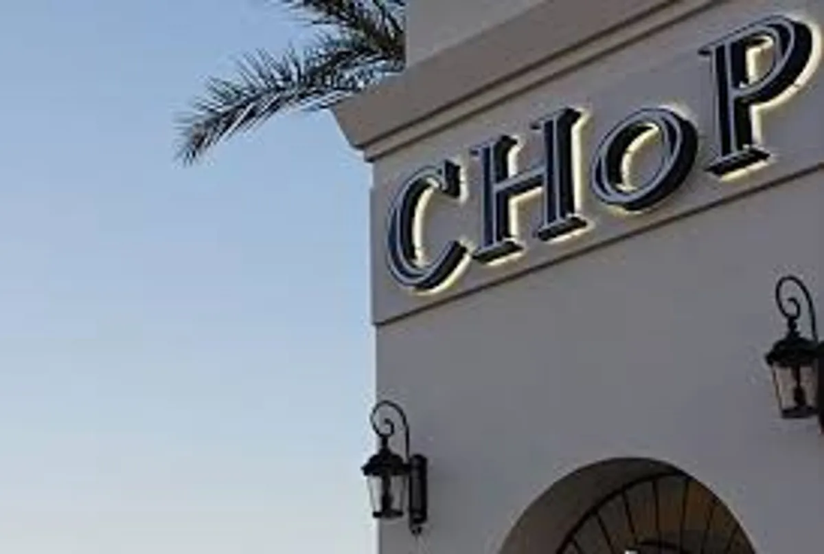This image captures a relaxed outdoor dining and gathering area, complete with palm trees, lanterns, and clear signage. The ambiance hints at communal social spaces and opportunities to enjoy sunset dinners or community events in a resort-like setting.