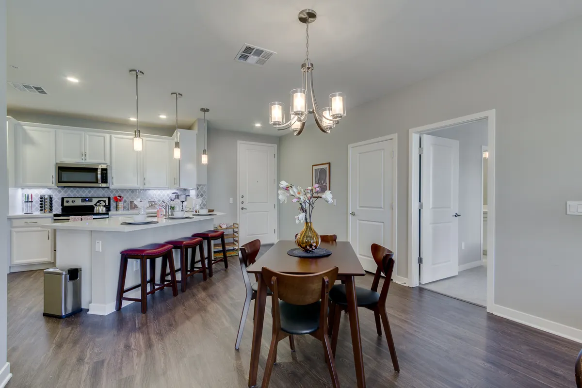 A welcoming open-plan space featuring a spacious dining table, kitchen island, elegant chandelier, and visible appliances. The layout highlights the seamless flow between the kitchen and dining areas, inviting gatherings and shared meals.