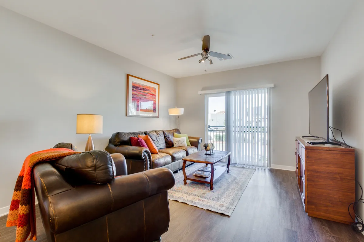 A cozy living room complete with a modern sofa, coffee table, large TV, stylish lamp, and eye-catching artwork. Sunlight streams into the room, creating a relaxing atmosphere perfect for unwinding, watching TV, or hosting friends.