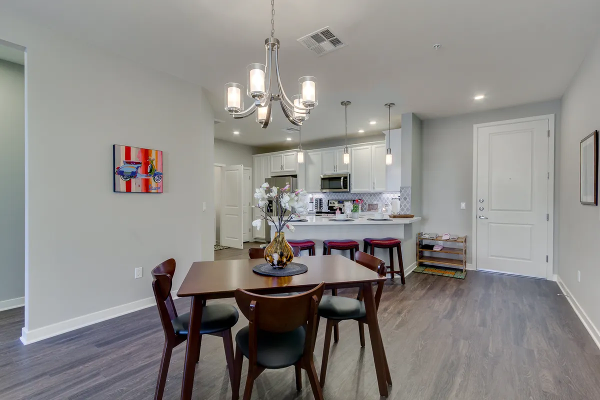 A cozy dining area with a stylish chandelier, modern kitchen island, and tasteful artwork adorning the wall. The scene is set for shared meals or social gatherings, evoking a sense of community and enjoyment.