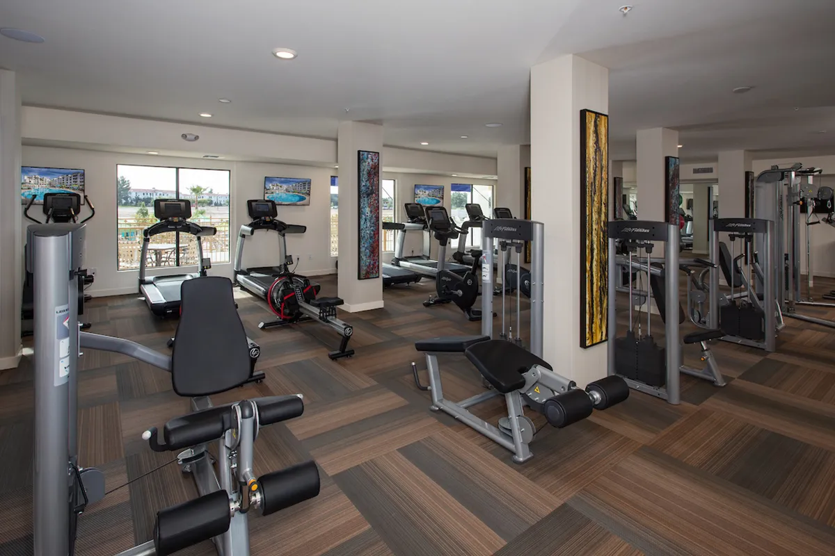 A spacious, modern gym with treadmills, weight machines, exercise benches, and vibrant wall art. The room is well-lit and designed to promote health and fitness, with ample room for group classes or personal workouts.