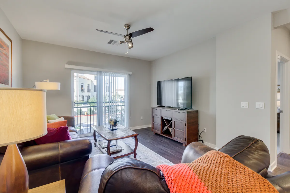 A comfortable living area featuring a plush sofa, coffee table, television, and sliding glass doors that likely open to a patio or outside area. The space is casual and inviting, filled with natural light.