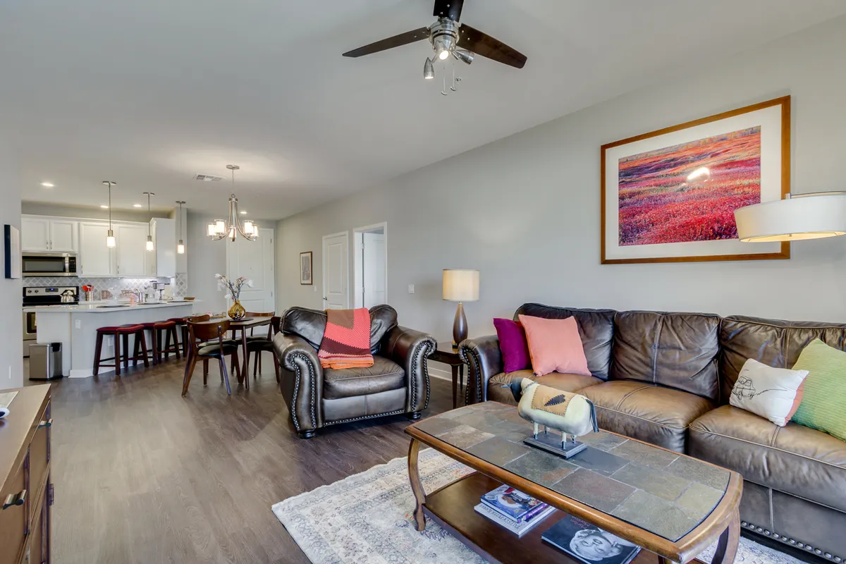 A warm, inviting living room featuring a leather sofa, vibrant throw pillows, a stylish coffee table, and modern artwork. The space is perfect for relaxing, socializing, or enjoying low-key activities with friends.