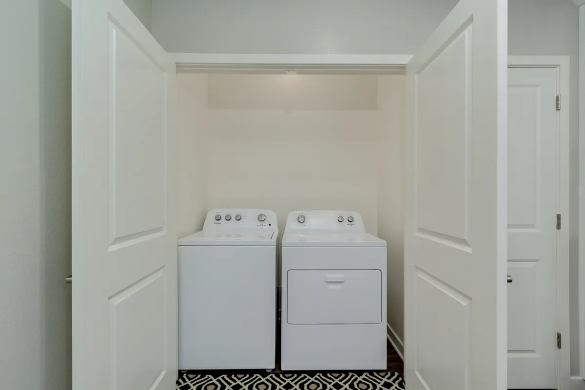 A practical laundry space with a full-size washer and dryer, geometric patterned floor, and a sense of order and efficiency. The area is clean and organized, supporting daily living with ease.
