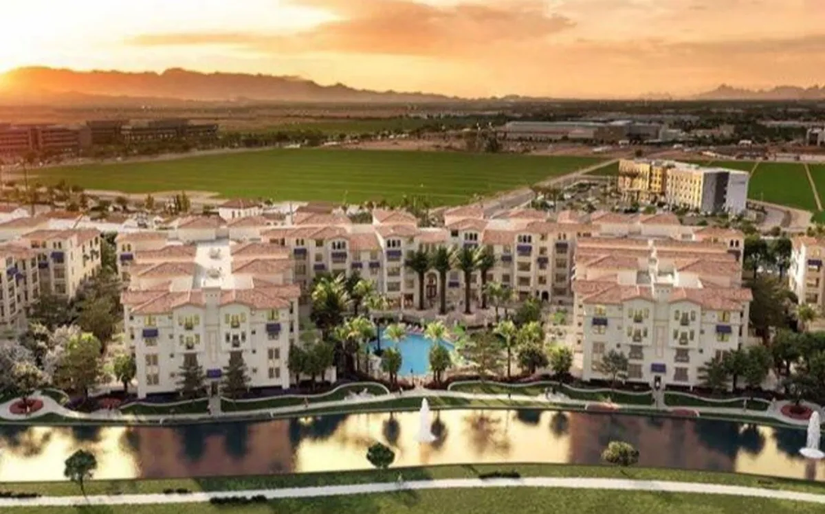 A beautifully landscaped resort-style outdoor area featuring a sparkling swimming pool with a sculptural fountain, surrounded by modern architecture and lush gardens. Lounge chairs and shaded seating arrangements invite relaxation and socializing, while the tranquil water adds a serene atmosphere.